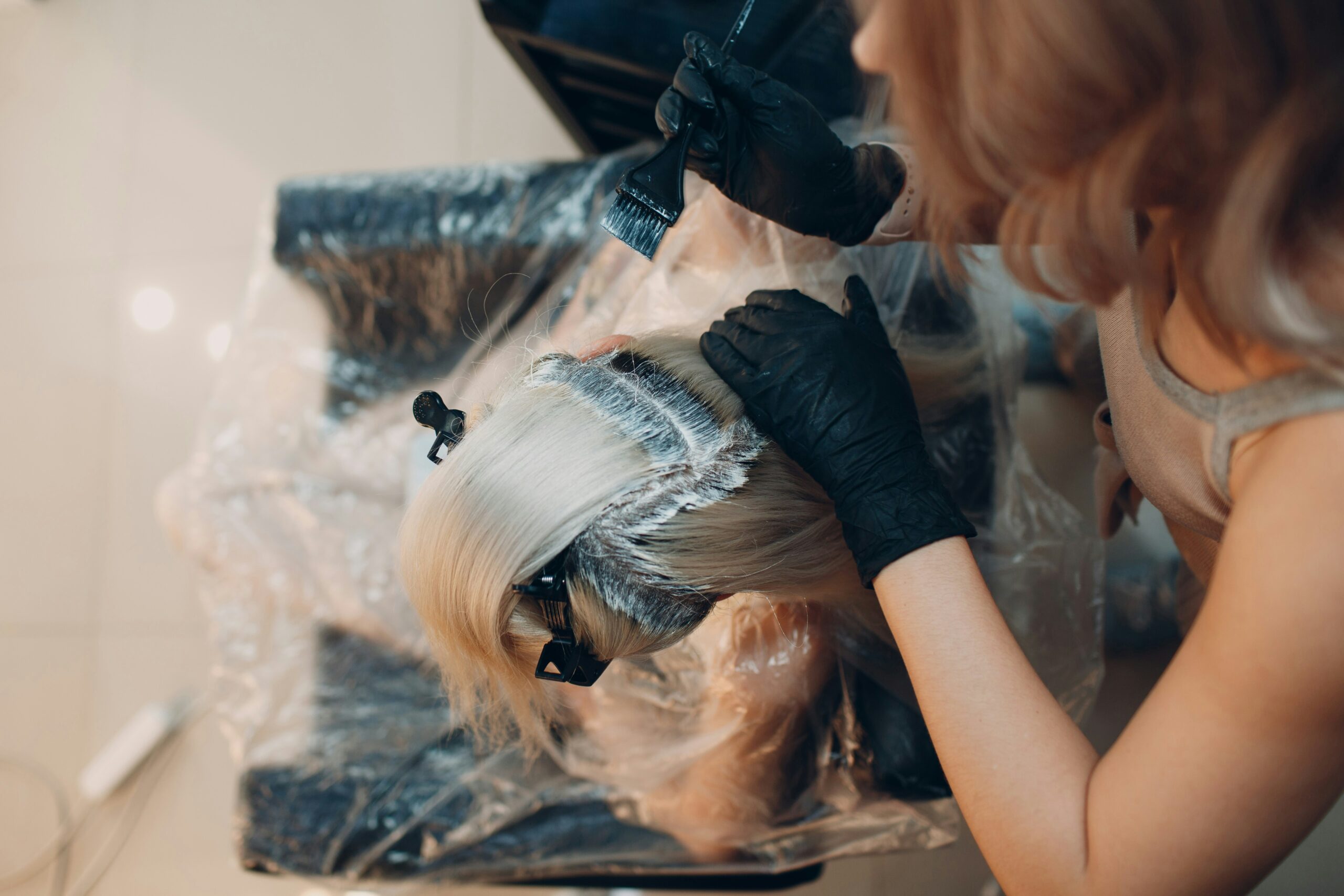 Stylist applying hair color with a brush to sectioned blonde hair at a salon.